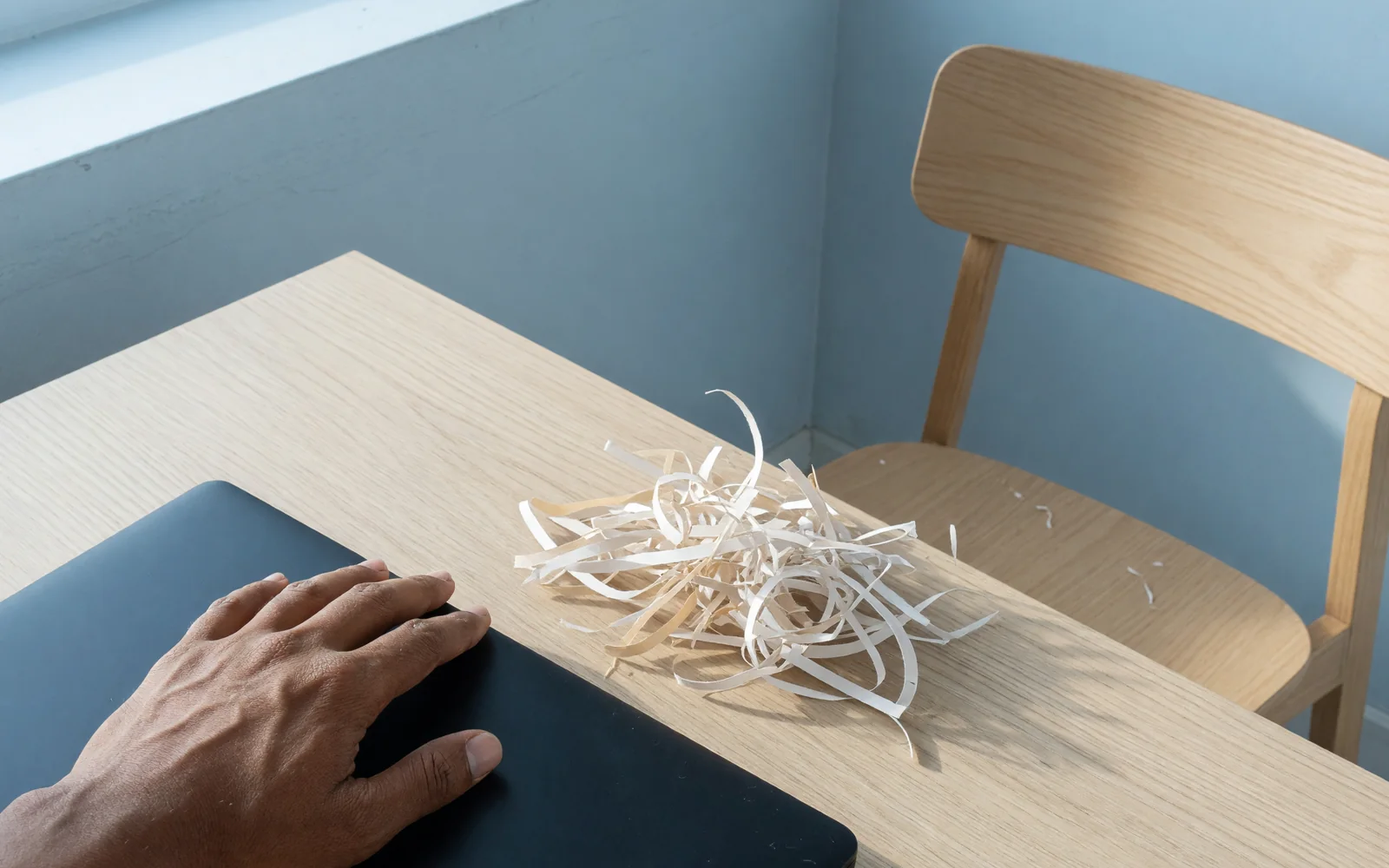 Closed laptop, shredded unreadable strips and a hand on the lid