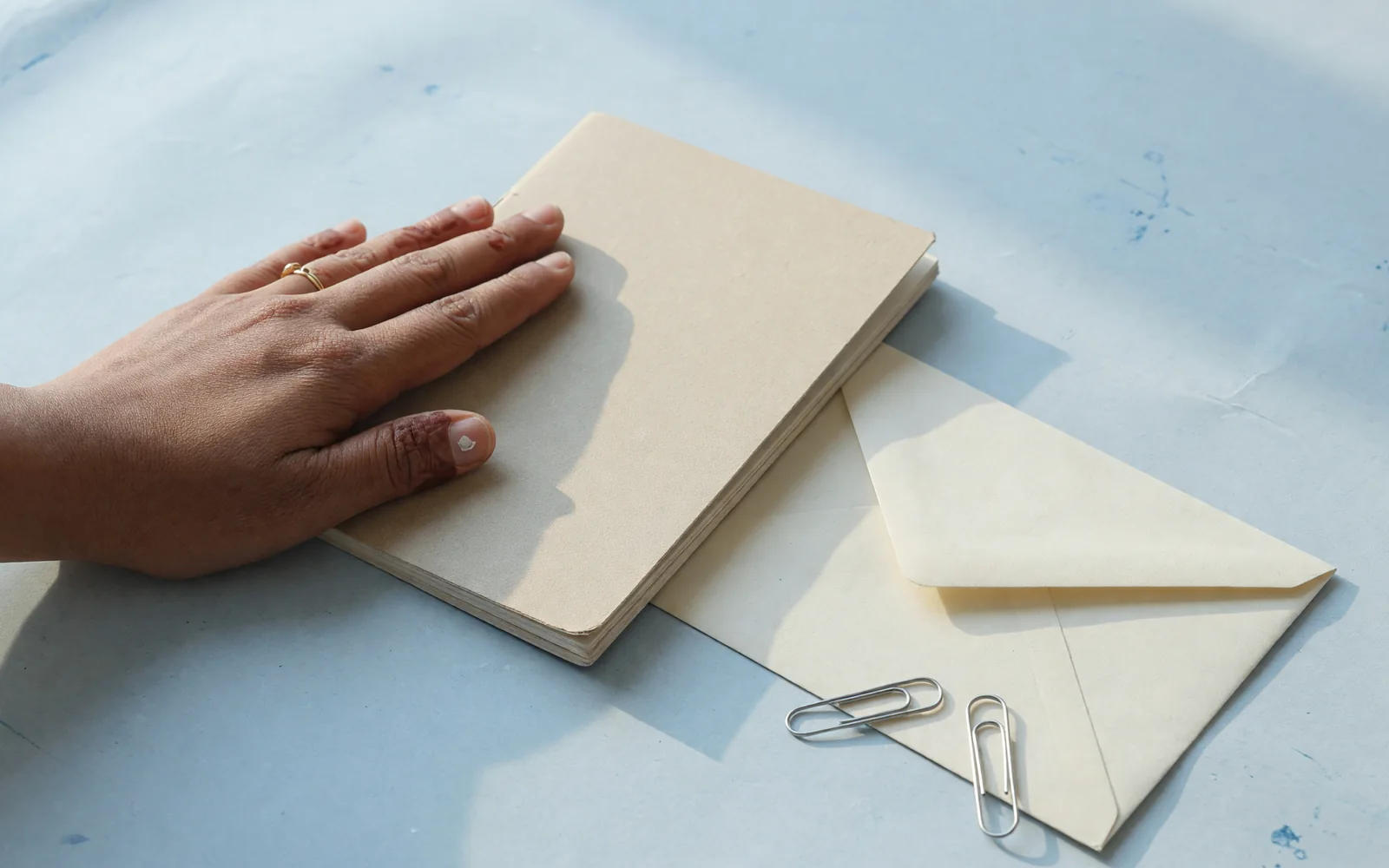 Closed booklet under a palm, clips and a blank envelope on ice-blue blotter