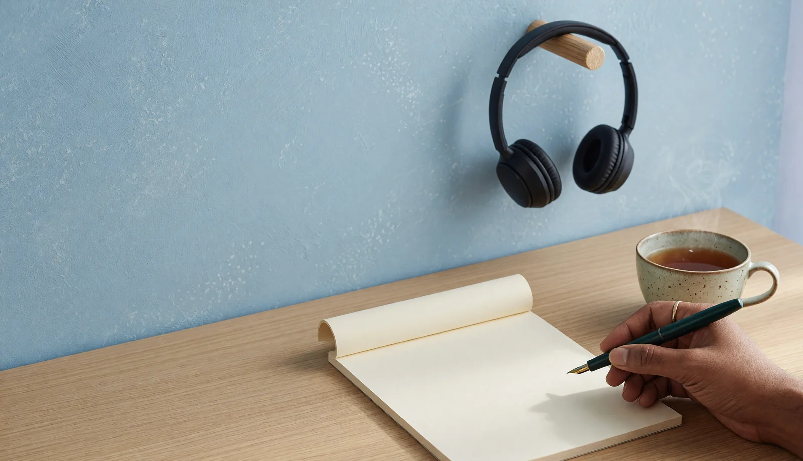 Headset on a peg, blank notepad and a hand making one unreadable stroke